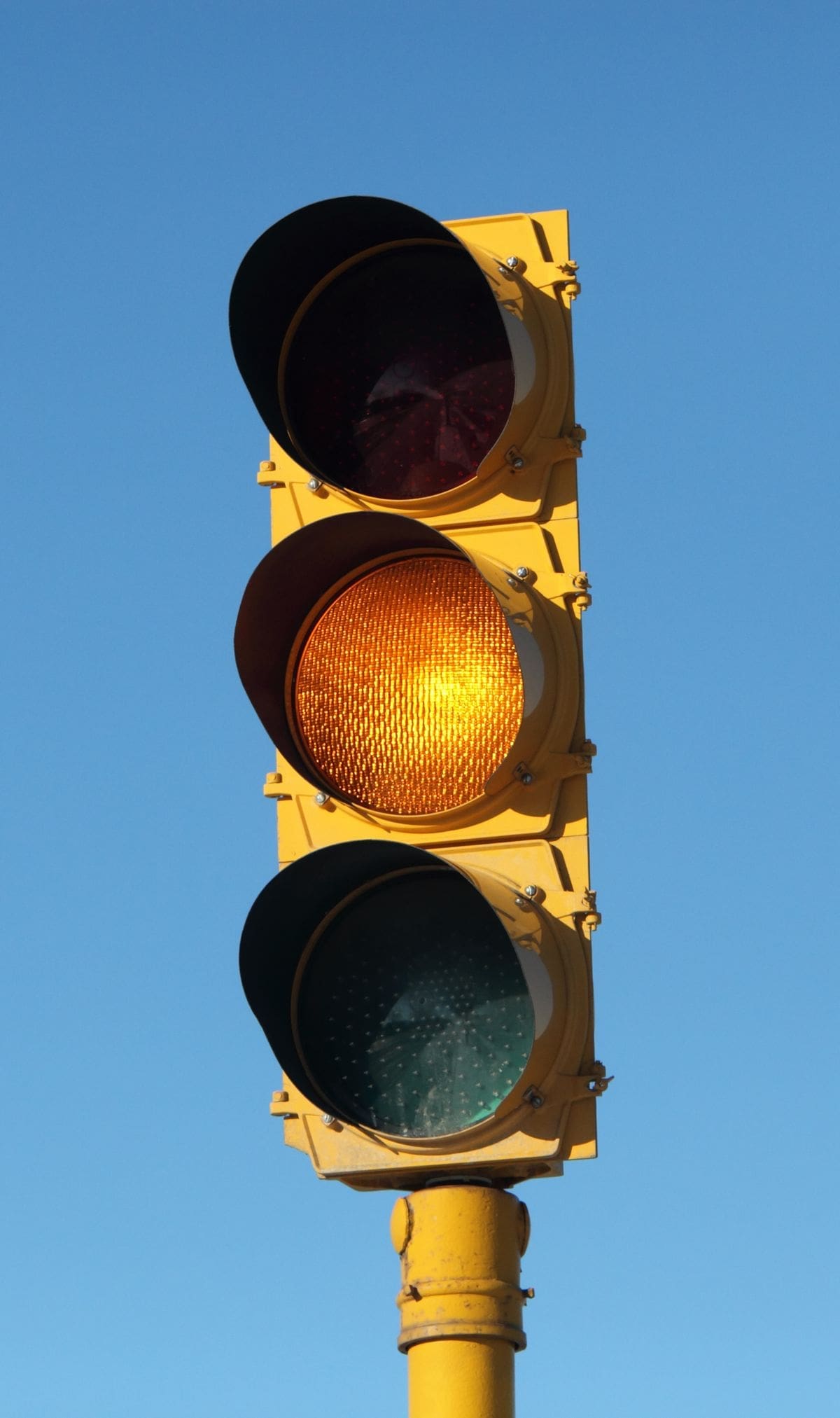 Yellow traffic light against a blue sky representing the pause educators need when limiting student learning beliefs surface in schools